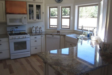 Example of a mid-sized classic u-shaped light wood floor and beige floor open concept kitchen design in San Diego with a farmhouse sink, glass-front cabinets, white cabinets, quartz countertops, white appliances, a peninsula and brown countertops