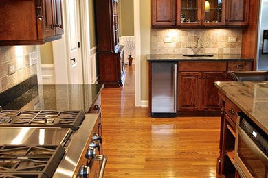 Example of a large classic u-shaped medium tone wood floor and brown floor eat-in kitchen design in Chicago with an undermount sink, raised-panel cabinets, dark wood cabinets, granite countertops, multicolored backsplash, travertine backsplash, stainless steel appliances, an island and brown countertops