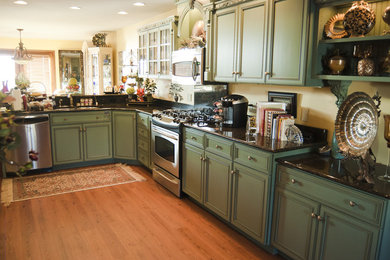 Example of a large farmhouse u-shaped medium tone wood floor eat-in kitchen design in Omaha with a double-bowl sink, beaded inset cabinets, green cabinets, granite countertops, black backsplash, stone slab backsplash, stainless steel appliances and a peninsula