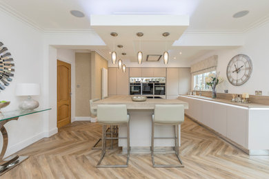 This is an example of a large contemporary l-shaped enclosed kitchen in Glasgow with flat-panel cabinets, beige cabinets, engineered stone countertops, black appliances, laminate floors, an island and white worktops.