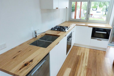 Idee per una cucina minimal di medie dimensioni con ante bianche, top in legno, parquet chiaro e nessuna isola