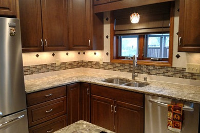 Inspiration for a large timeless l-shaped enclosed kitchen remodel in Milwaukee with a double-bowl sink, raised-panel cabinets, dark wood cabinets, granite countertops, beige backsplash, ceramic backsplash, stainless steel appliances, an island and gray countertops