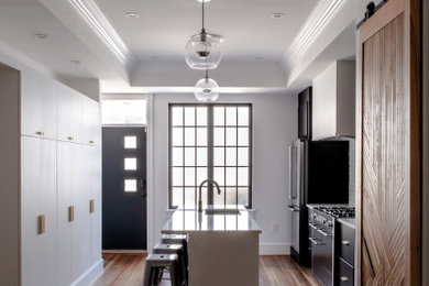 Example of a mid-sized trendy galley medium tone wood floor, brown floor and tray ceiling eat-in kitchen design in Baltimore with an undermount sink, flat-panel cabinets, black cabinets, quartz countertops, white backsplash, brick backsplash, stainless steel appliances, an island and white countertops