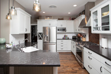 Example of a mid-sized transitional medium tone wood floor open concept kitchen design in Portland with a farmhouse sink, shaker cabinets, white cabinets, quartz countertops, white backsplash, subway tile backsplash, stainless steel appliances and an island
