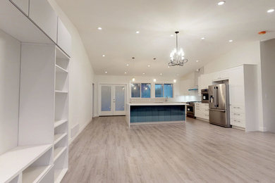 Example of a large trendy l-shaped laminate floor and brown floor open concept kitchen design in Vancouver with recessed-panel cabinets, white cabinets, solid surface countertops, white backsplash, an island, white countertops, an undermount sink, ceramic backsplash and stainless steel appliances