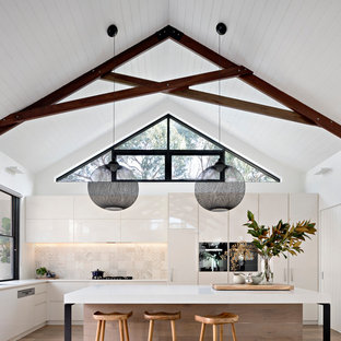 Photo of a mid-sized contemporary l-shaped kitchen in Melbourne with flat-panel cabinets, white cabinets, beige splashback, medium hardwood floors, brown floor, an undermount sink, panelled appliances and with island.