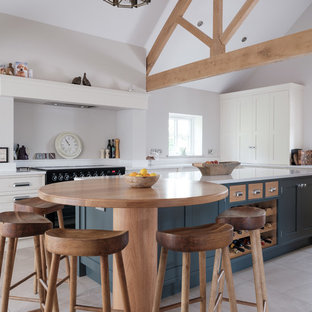 Photo of a large farmhouse kitchen in Cheshire with quartz worktops, porcelain flooring, an island, white worktops, a belfast sink, shaker cabinets, white cabinets, black appliances and beige floors.