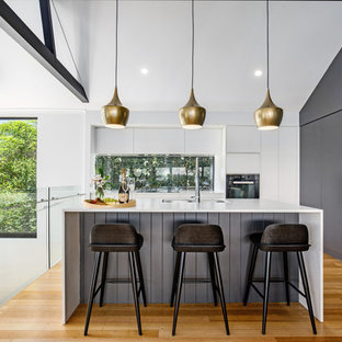 Mid-sized contemporary l-shaped open plan kitchen in Sunshine Coast with an undermount sink, flat-panel cabinets, quartz benchtops, window splashback, with island, white benchtop, white cabinets, panelled appliances, medium hardwood floors and brown floor.