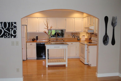 Mid-sized elegant l-shaped light wood floor enclosed kitchen photo in Minneapolis with a double-bowl sink, recessed-panel cabinets, white cabinets, laminate countertops, white appliances and an island
