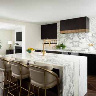 This is an example of a medium sized contemporary galley kitchen/diner in London with a built-in sink, flat-panel cabinets, dark wood cabinets, marble worktops, white splashback, marble splashback, stainless steel appliances, dark hardwood flooring, an island, brown floors and white worktops.