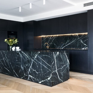 Photo of a contemporary kitchen in Sydney with flat-panel cabinets, black cabinets, black splashback, stone slab splashback, light hardwood floors, with island, beige floor, black benchtop and panelled appliances.