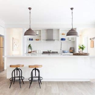 Inspiration for a mid-sized transitional galley kitchen in Melbourne with white splashback, ceramic splashback, light hardwood floors, with island, brown floor, white benchtop, an undermount sink, open cabinets, white cabinets and stainless steel appliances.