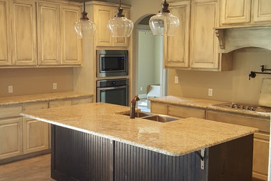 This is an example of a medium sized traditional l-shaped open plan kitchen in Austin with a belfast sink, raised-panel cabinets, white cabinets, granite worktops, stainless steel appliances, medium hardwood flooring, an island and brown floors.