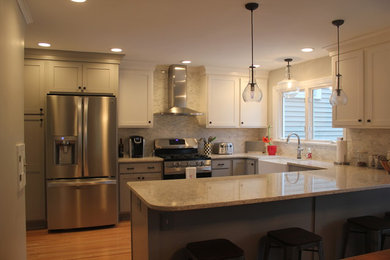 Large u-shaped light wood floor eat-in kitchen photo in New York with a farmhouse sink, gray cabinets, solid surface countertops, stainless steel appliances, recessed-panel cabinets, gray backsplash and a peninsula