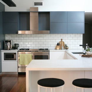Contemporary u-shaped kitchen in Sydney with an undermount sink, flat-panel cabinets, blue cabinets, white splashback, subway tile splashback, stainless steel appliances, dark hardwood floors, a peninsula, brown floor and white benchtop.