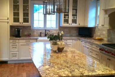 Example of a large classic l-shaped light wood floor eat-in kitchen design in New York with an island, recessed-panel cabinets, white cabinets, granite countertops, beige backsplash, stone tile backsplash, stainless steel appliances and a farmhouse sink