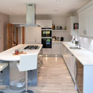 Medium sized traditional l-shaped enclosed kitchen in London with porcelain flooring, beige floors, a double-bowl sink, white cabinets, an island, white worktops, shaker cabinets, white splashback and black appliances.