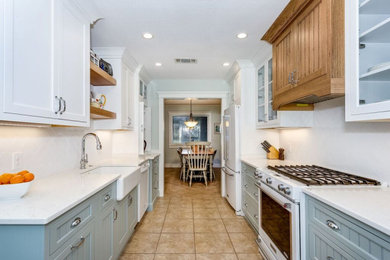 Example of a mid-sized beach style galley porcelain tile and brown floor eat-in kitchen design in Other with a farmhouse sink, beaded inset cabinets, white cabinets, quartz countertops, white backsplash, subway tile backsplash, white appliances, no island and white countertops