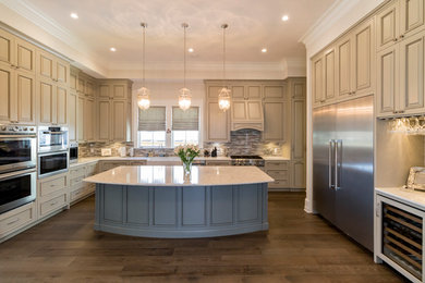 Eat-in kitchen - large traditional u-shaped medium tone wood floor eat-in kitchen idea in Miami with a farmhouse sink, raised-panel cabinets, beige cabinets, solid surface countertops, beige backsplash, glass tile backsplash, stainless steel appliances and an island