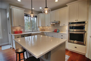 Example of a large trendy l-shaped medium tone wood floor and brown floor open concept kitchen design in Portland with an undermount sink, white cabinets, quartz countertops, gray backsplash, subway tile backsplash, stainless steel appliances and an island