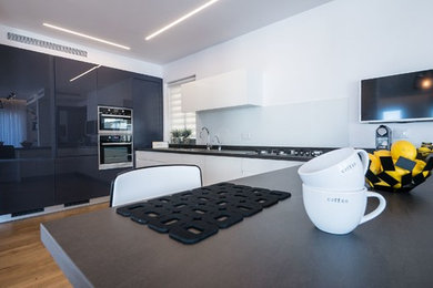 Immagine di una cucina moderna con lavello da incasso, ante nere, paraspruzzi con lastra di vetro e elettrodomestici da incasso