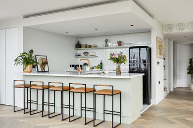 This is an example of a medium sized contemporary galley open plan kitchen in London with black appliances, a built-in sink, flat-panel cabinets, green cabinets, composite countertops, an island and multicoloured worktops.