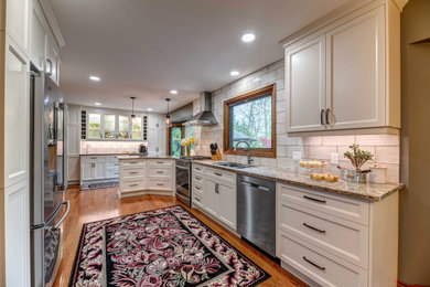 Example of a transitional u-shaped medium tone wood floor and brown floor kitchen design in Other with an undermount sink, recessed-panel cabinets, white cabinets, white backsplash, a peninsula and brown countertops
