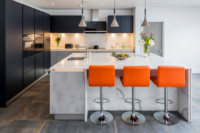 Photo of a medium sized contemporary l-shaped open plan kitchen in London with flat-panel cabinets, blue cabinets, quartz worktops, white splashback, marble splashback, black appliances, an island, brown floors, white worktops and a submerged sink.