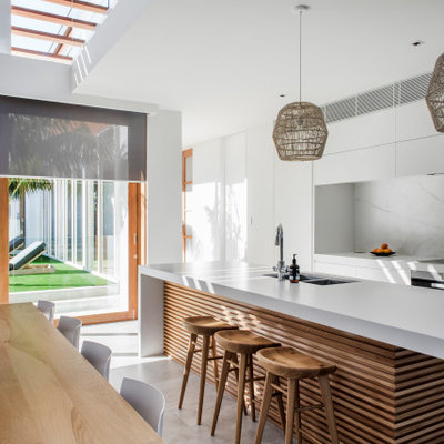 Beach style galley gray floor kitchen photo in Sunshine Coast with an undermount sink, flat-panel cabinets, white cabinets, white backsplash, paneled appliances, an island and white countertops