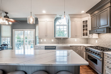 Inspiration for a large contemporary u-shaped medium tone wood floor and brown floor open concept kitchen remodel in Philadelphia with a farmhouse sink, raised-panel cabinets, white cabinets, marble countertops, gray backsplash, ceramic backsplash, stainless steel appliances, an island and white countertops
