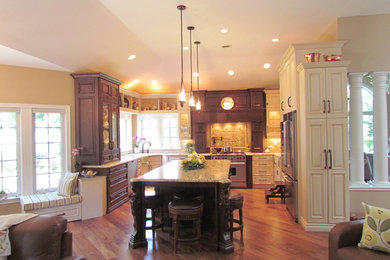 Eat-in kitchen - large traditional u-shaped medium tone wood floor and brown floor eat-in kitchen idea in Other with raised-panel cabinets, granite countertops, beige backsplash, travertine backsplash, stainless steel appliances, an island and dark wood cabinets