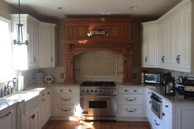 Example of a mid-sized classic u-shaped medium tone wood floor and brown floor open concept kitchen design in Other with a farmhouse sink, recessed-panel cabinets, white cabinets, granite countertops, beige backsplash, limestone backsplash, stainless steel appliances and an island