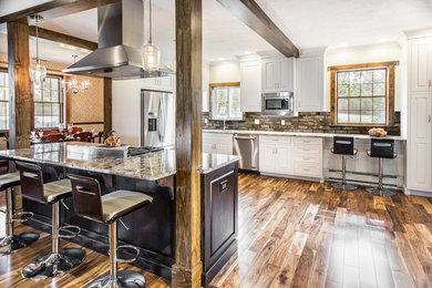 Example of a large transitional l-shaped medium tone wood floor and brown floor kitchen design in Other with an undermount sink, raised-panel cabinets, white cabinets, granite countertops, brown backsplash, stainless steel appliances and an island