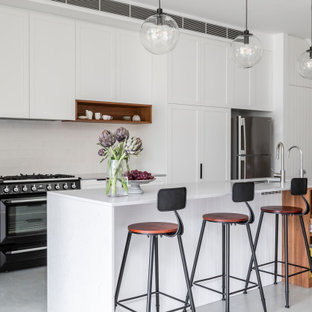 Inspiration for a mid-sized transitional single-wall open plan kitchen in Sydney with an undermount sink, shaker cabinets, white cabinets, quartz benchtops, white splashback, ceramic splashback, black appliances, concrete floors, with island, grey floor and grey benchtop.