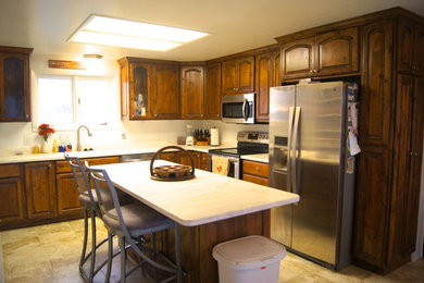 Example of a large classic l-shaped ceramic tile and beige floor eat-in kitchen design in Salt Lake City with a double-bowl sink, raised-panel cabinets, dark wood cabinets, solid surface countertops, stainless steel appliances and an island