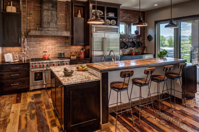 Example of a large mountain style l-shaped medium tone wood floor and brown floor kitchen design in Denver with an undermount sink, shaker cabinets, dark wood cabinets, stainless steel appliances, an island, red backsplash, brick backsplash and black countertops