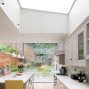 Classic galley kitchen in London with a submerged sink, shaker cabinets, white cabinets, light hardwood flooring, an island, beige floors and white worktops.