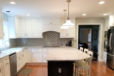 Large transitional l-shaped medium tone wood floor and brown floor eat-in kitchen photo in Baltimore with a farmhouse sink, recessed-panel cabinets, white cabinets, gray backsplash, ceramic backsplash, stainless steel appliances, an island, white countertops and granite countertops