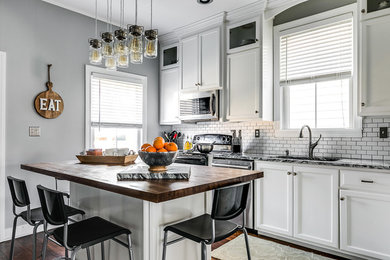 Example of a transitional single-wall dark wood floor and brown floor kitchen design in Richmond with recessed-panel cabinets, white cabinets, wood countertops, white backsplash, subway tile backsplash, stainless steel appliances and an island