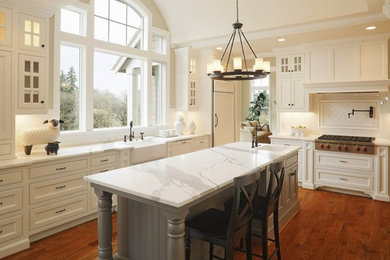 Example of a cottage l-shaped medium tone wood floor and brown floor enclosed kitchen design in Charlotte with a farmhouse sink, recessed-panel cabinets, white cabinets, marble countertops, white backsplash, subway tile backsplash, an island and paneled appliances