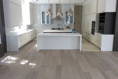 Example of a large trendy u-shaped light wood floor eat-in kitchen design in Miami with an undermount sink, flat-panel cabinets, white cabinets, quartzite countertops, paneled appliances and two islands
