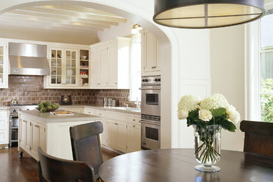 Klassisk inredning av ett stort kök, med vita skåp, brunt stänkskydd, rostfria vitvaror, luckor med infälld panel, en undermonterad diskho, granitbänkskiva, stänkskydd i porslinskakel, mellanmörkt trägolv och en köksö