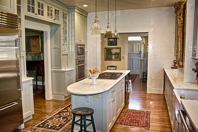 Inspiration for a mid-sized timeless u-shaped medium tone wood floor eat-in kitchen remodel in Other with a farmhouse sink, quartzite countertops, white backsplash, ceramic backsplash, stainless steel appliances, an island, flat-panel cabinets and green cabinets