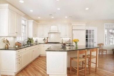 Inspiration for a large timeless l-shaped medium tone wood floor eat-in kitchen remodel in New York with an undermount sink, raised-panel cabinets, white cabinets, granite countertops, white backsplash, subway tile backsplash, paneled appliances and an island
