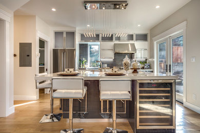 Mid-sized trendy single-wall light wood floor open concept kitchen photo in Other with louvered cabinets, an island, gray cabinets, solid surface countertops, metallic backsplash, metal backsplash, stainless steel appliances and a drop-in sink