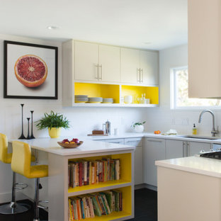 Immagine di una piccola cucina moderna con lavello sottopiano, nessun'anta, ante gialle, top in quarzite, paraspruzzi bianco, paraspruzzi con piastrelle in ceramica, elettrodomestici in acciaio inossidabile, pavimento in cementine, penisola, pavimento nero e top bianco