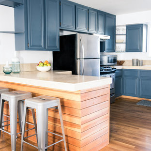 Design ideas for a transitional l-shaped eat-in kitchen in Los Angeles with a double-bowl sink, raised-panel cabinets, blue cabinets, limestone benchtops, beige splashback, stone slab splashback, stainless steel appliances, medium hardwood floors and a peninsula.