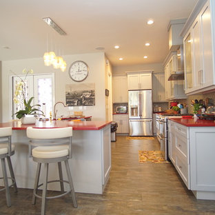 This is an example of a large transitional galley open plan kitchen in Miami with a farmhouse sink, shaker cabinets, grey cabinets, quartzite benchtops, beige splashback, glass tile splashback, stainless steel appliances, porcelain floors, with island, multi-coloured floor and red benchtop.