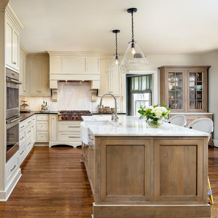 Inspiration for a timeless l-shaped medium tone wood floor and brown floor kitchen remodel in New Orleans with a farmhouse sink, shaker cabinets, beige cabinets, stainless steel appliances, an island and black countertops