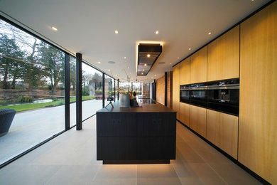 Exemple d'une grande cuisine linéaire tendance en bois clair avec un placard à porte plane, un sol en calcaire, îlot, un sol gris et plan de travail noir.